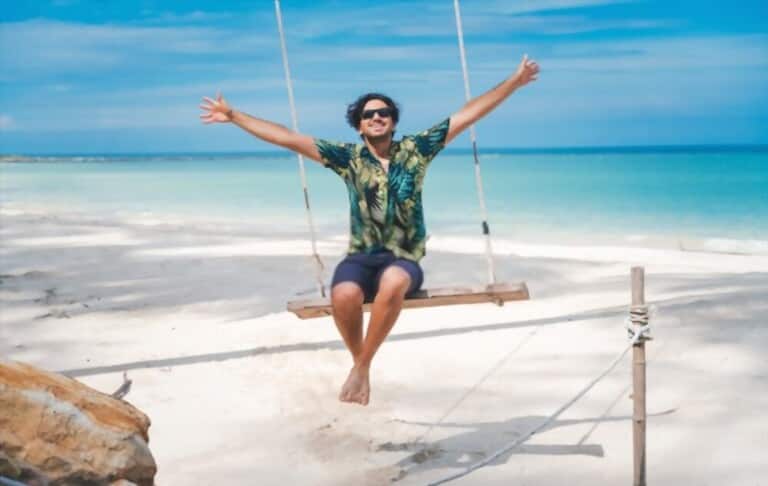 young man with Hawaiian shirt sitting on swing by the beach