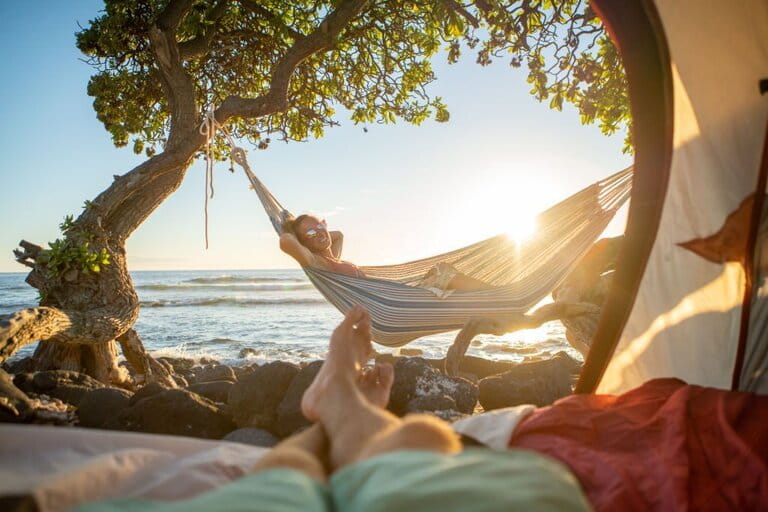 View of foot man from inside a beach camping tent in Hawaii looking at his girlfriend in an outdoor hammock with cool weather and mild sunshine