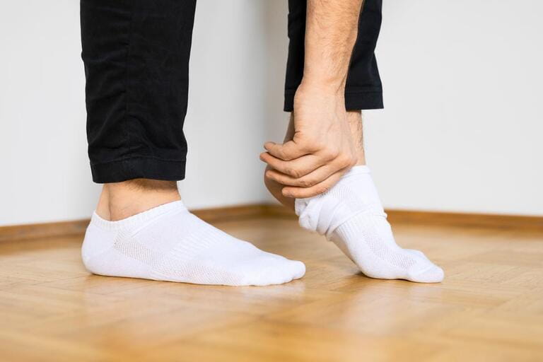 human feet putting on white ankle socks by hand standing on wooden floor human feet putting on white ankle socks by hand standing on wooden floor