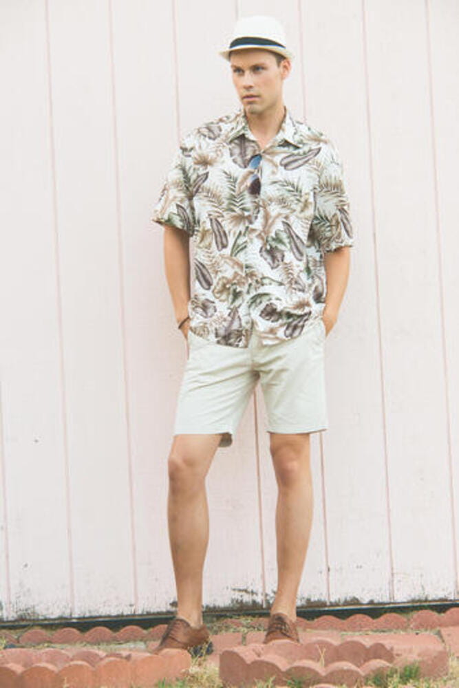 A handsome man, male model posing in Summer Clothes outdoor standing against a plain wooden wall. He wears a white hat. A handsome man, male model posing in Summer Clothes outdoor standing against a plain wooden wall. He wears a white hat.