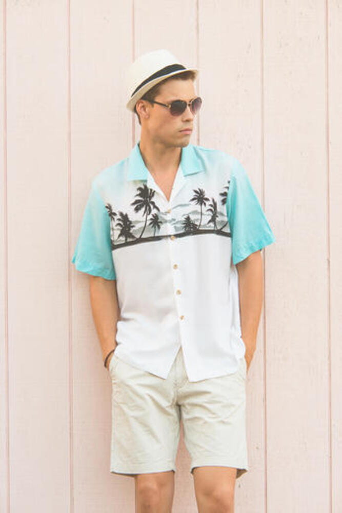 A handsome male model posing in Summer Clothes outdoor against a plain wooden wall. He wears a white fedora hat and aviator sunglasses. A handsome male model posing in Summer Clothes outdoor against a plain wooden wall. He wears a white fedora hat and aviator sunglasses.