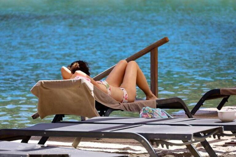 Woman in bikini sunbathes lying in lounge chair on sea background. Beach vacation on tourist resort Woman in bikini sunbathes lying in lounge chair on sea background. Beach vacation on tourist resort