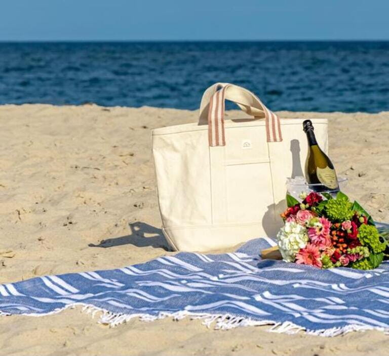 Still life on a Hampton's beach consisting of a beach blanket, champagne and flowers