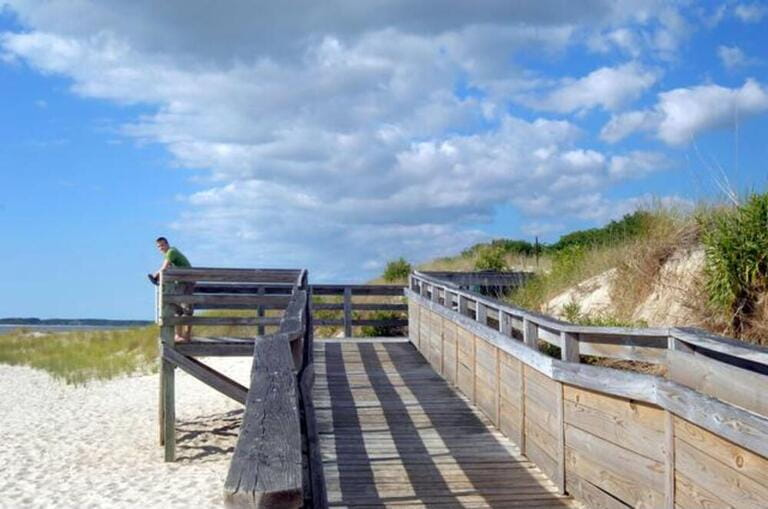 Young man stands barefoot on a weathered dock on the beach at Cape Charles, Virginia. A bank of clouds forms overhead and vivid blue fills the skies. Young man stands barefoot on a weathered dock on the beach at Cape Charles, Virginia. A bank of clouds forms overhead and vivid blue fills the skies.