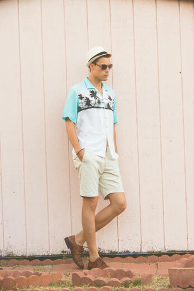 A handsome male model posing in Summer Clothes outdoor standing against a plain wooden wall. A handsome male model posing in Summer Clothes outdoor standing against a plain wooden wall.