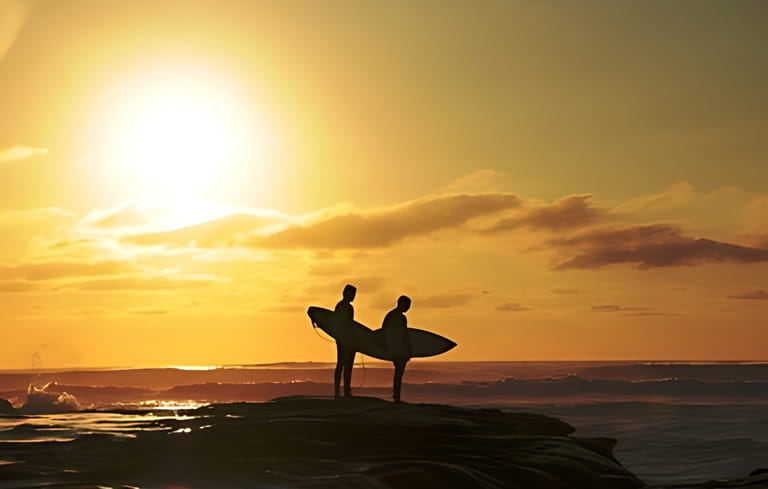 Surfer couple in silhouette holding surf boards at sunset