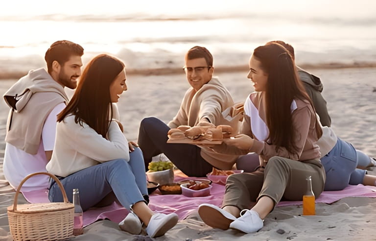 friendship, leisure and fast food concept - group of happy friends eating sandwiches or burgers at picnic on beach in summer friendship, leisure and fast food concept - group of happy friends eating sandwiches or burgers at picnic on beach in summer