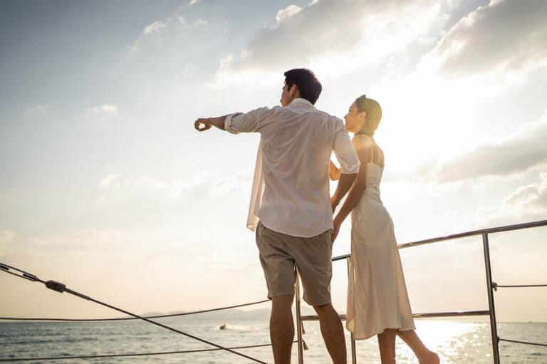 Beautiful Asian couple drinking champagne while partying on a yacht. Attractive man and woman hanging out, celebrating anniversary honeymoon trip