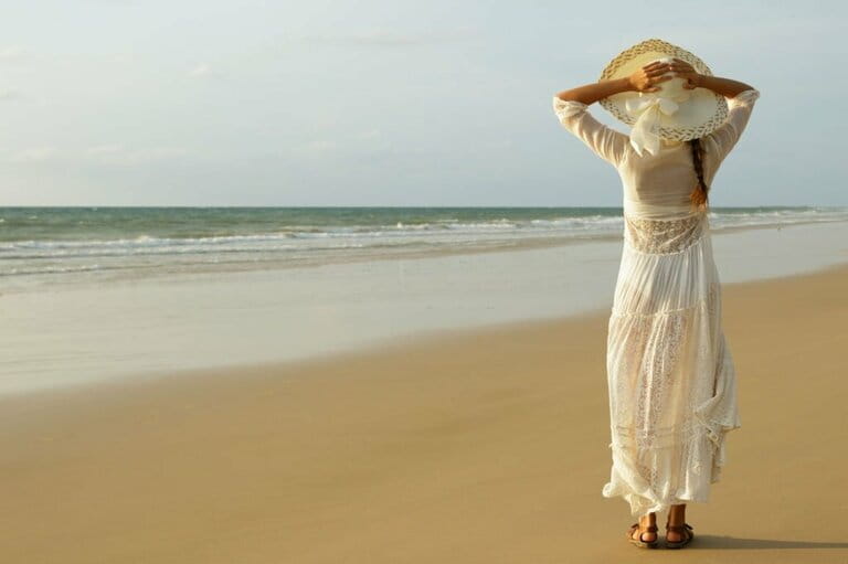 Woman in beautiful white dress walking on the beach during sunset Woman in beautiful white dress walking on the beach during sunset