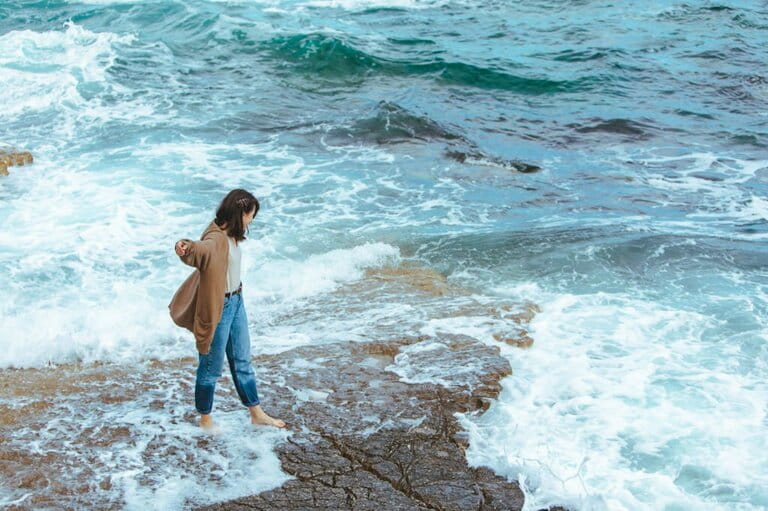 Woman walking by rocky beach in wet jeans bare feet Woman walking by rocky beach in wet jeans bare feet