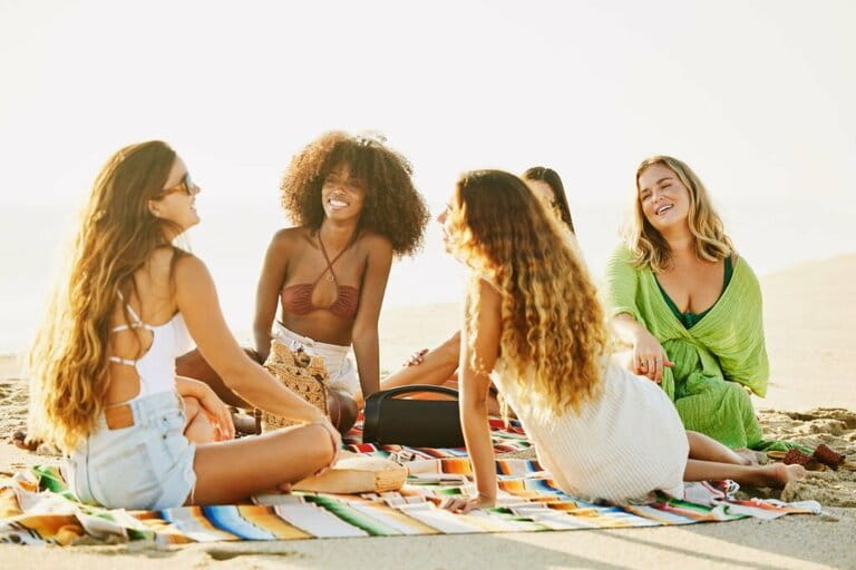 Wide shot of female friends relaxing on blanket on tropical beach Wide shot of female friends relaxing on blanket on tropical beach