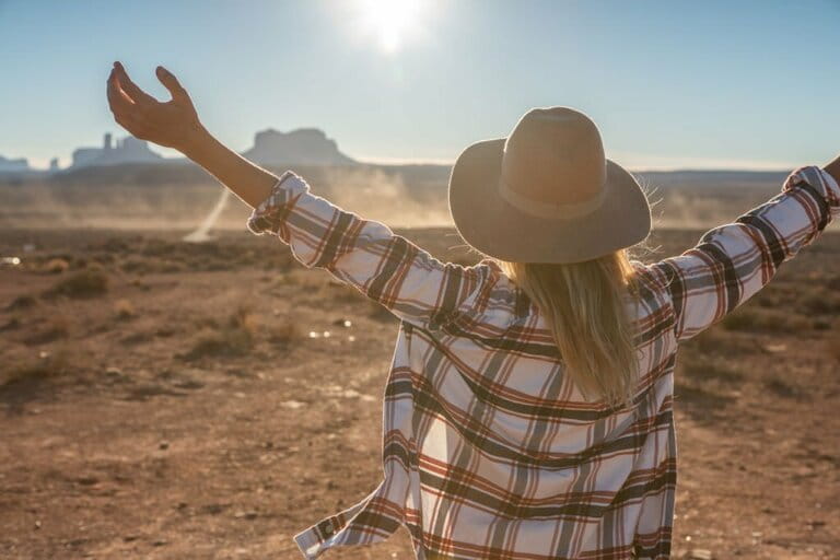 Rear view of woman standing on long road leading to Monument Valley in USA. People travel to America