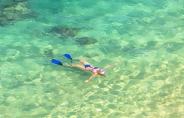 Woman snorkeling over coral reef in Hanauma Bay Nature Preserve, Oahu, Hawaii, USA. Female lying above the crystalline water in tropical sea with american flag bikini. Watersport activity in Hawaii.