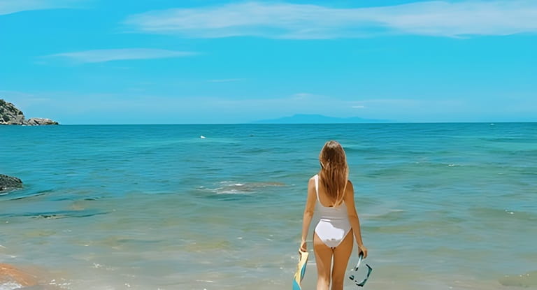 Back view of woman in bikini, carrying snorkel gear towards the ocean. Get set for an amazing snorkeling experience. Concept of tropical summer vacation.