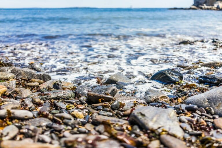 Rocky public beach called Ship Cove by Portland Head Lighthouse in Cape Elizabeth, Maine with close-up of water and rocks at ground level