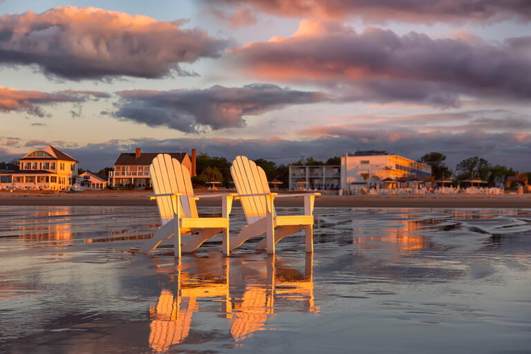 Two wooden traditional armchairs on a sandy beach at sunrise overlooking the coastline. Atlantic Ocean. USA. Maine. Old Orchard Beach. Two wooden traditional armchairs on a sandy beach at sunrise overlooking the coastline. Atlantic Ocean. USA. Maine. Old Orchard Beach.