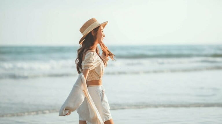 Summer beach vacation concept, Young woman wearing hat walking on ocean beach on hot summer day, Summer travel and relaxation